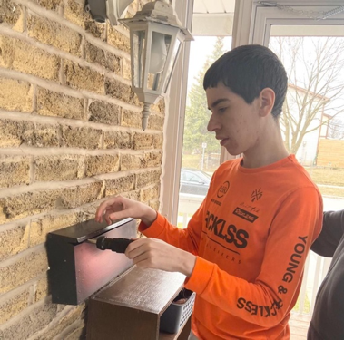 a special ed students using a screwdriver to attach a mailbox to a house