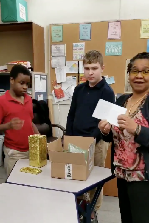 a special education teacher standing with her students while opening a holiday gift