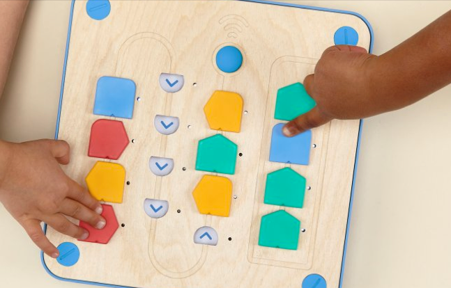 a student's finger pointing at the cubetto robot logic blocks in the board 
