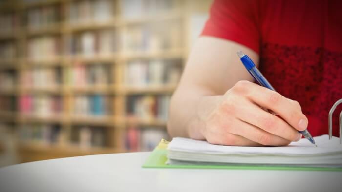 a student writes with a pen in a school library