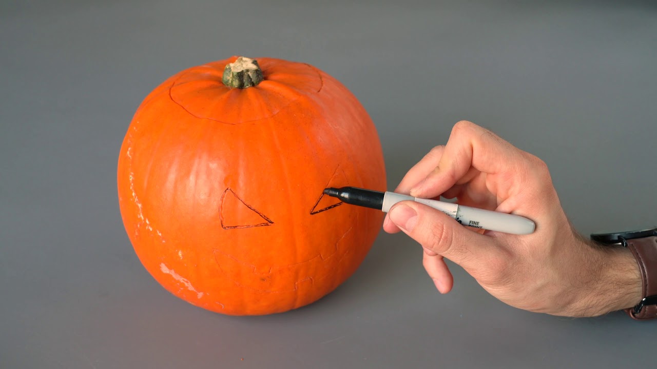 a person drawing eyes on a pumpkin with a marker