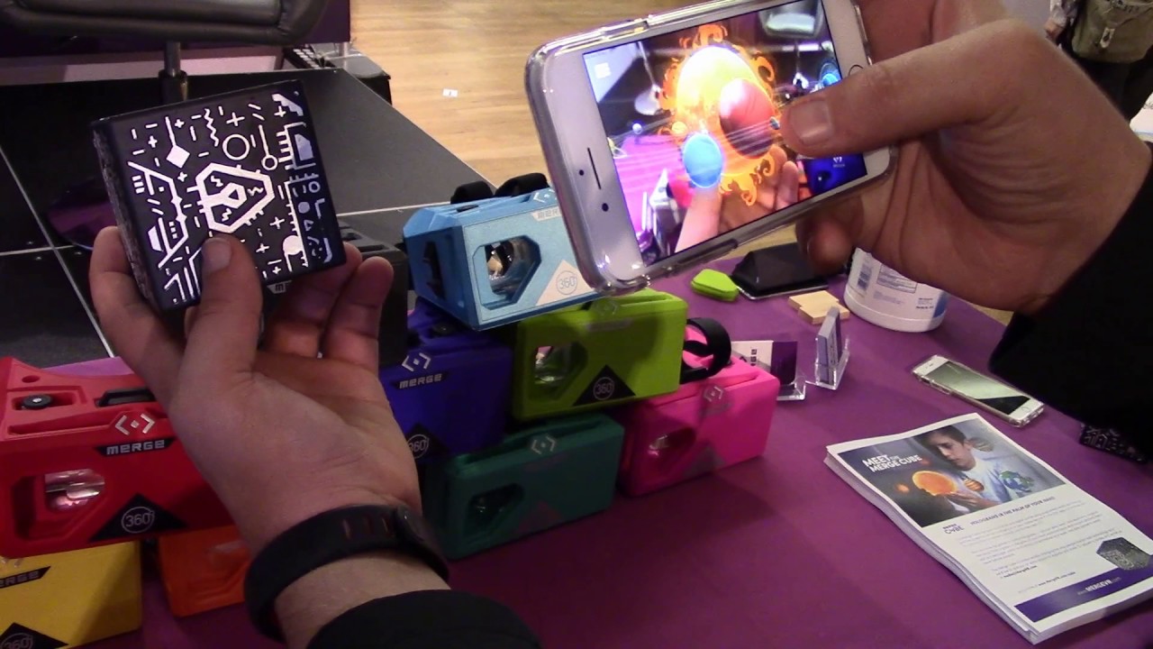 a person holding a merge cube and a mobile device for AR viewing