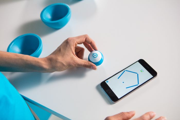 a person holding a blue sphero mini robot between their fingers while working with the sphero edu app