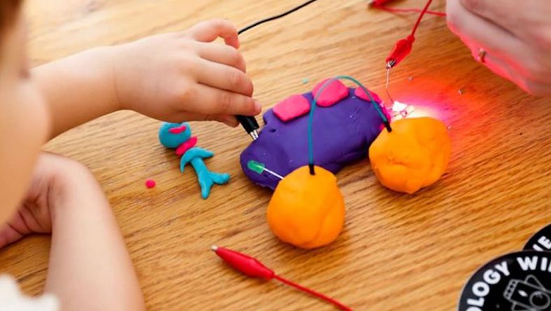 a young student connecting an alligator clip to an electro dough circuit 