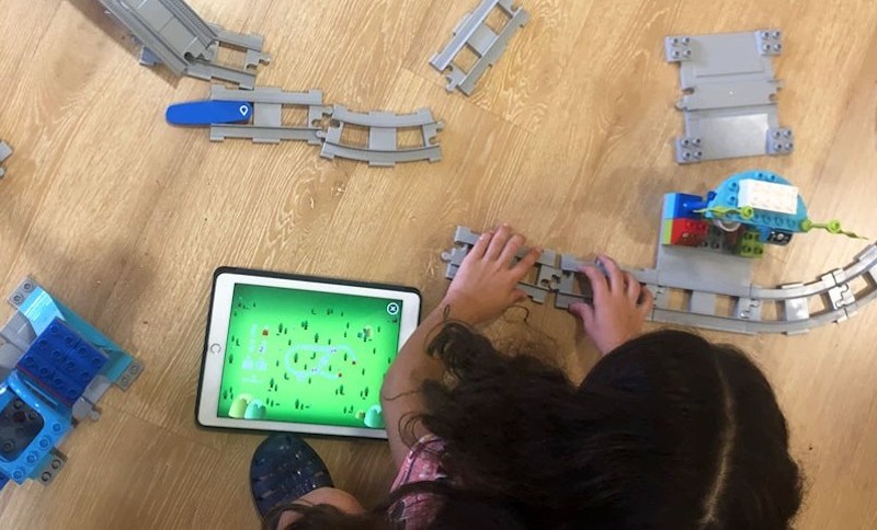 a student building a train track before running a program in a coding education class