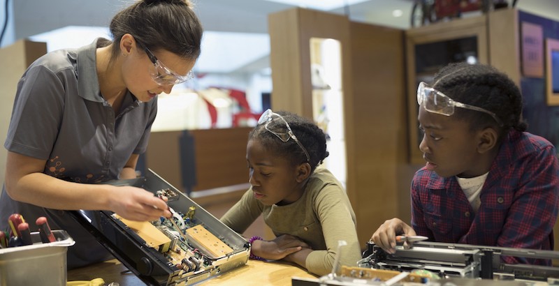 students watch as their teacher shows them an electronics board as part of helping them develop a STEM mindset for problem solving