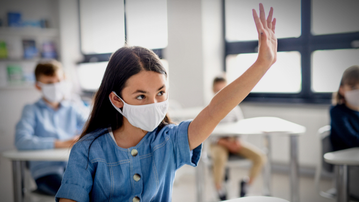 a student wearing a mask in the classroom raises her hand after returning to school amid discussions about learning loss