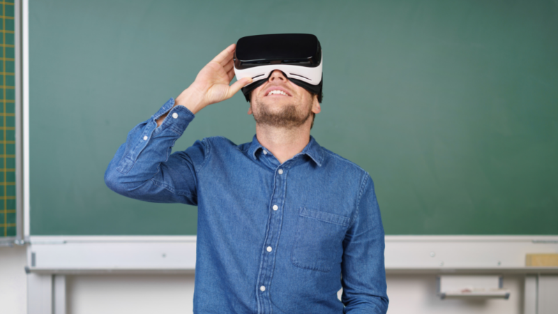 a teacher looking into a virtual reality headset in a classroom