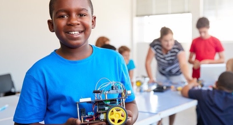 a child holding a robot in his hands as a teacher works on scaling STEM activities for students