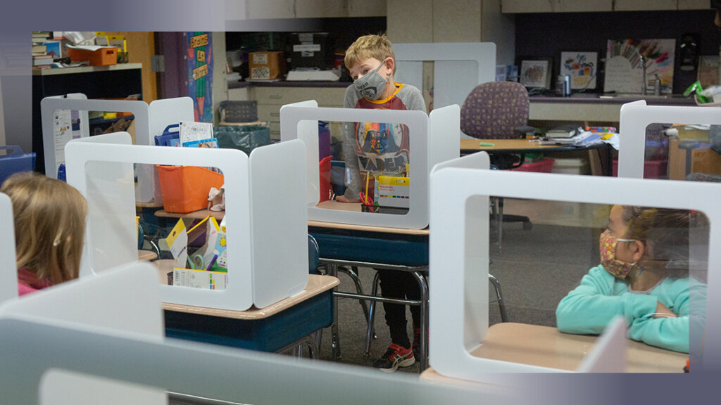 students sit at desks behind clear dividers in an effort to ensure safety upon returning to the classroom and addressing SEL