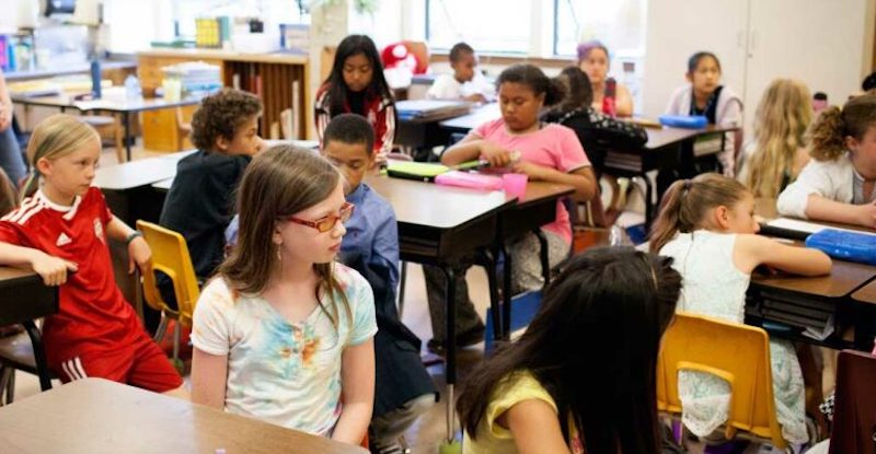 elementary students listening as a teacher speaks in a self-paced learning classroom
