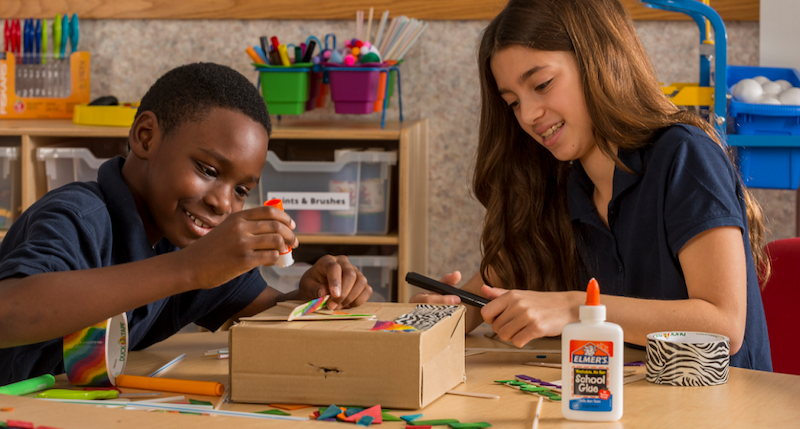 two students working on an art project with glue and cardboard in a school makerspace