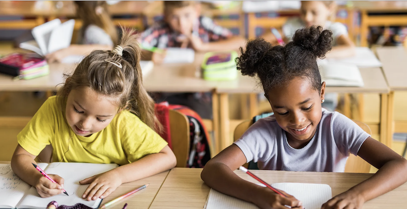 two young students writing with pens in the classroom to promote SEL and equity