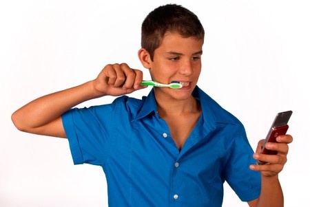 a teenager brushing his teeth while looking at a cellphone and texting