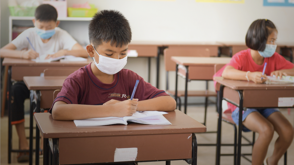 students writing with pens while wearing masks following an end to distance learning