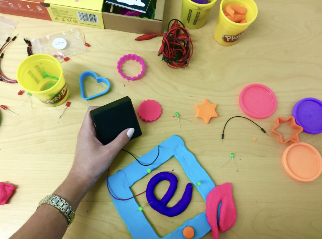 a hand holding a battery component with the electro dough components and eduporium logo on the table