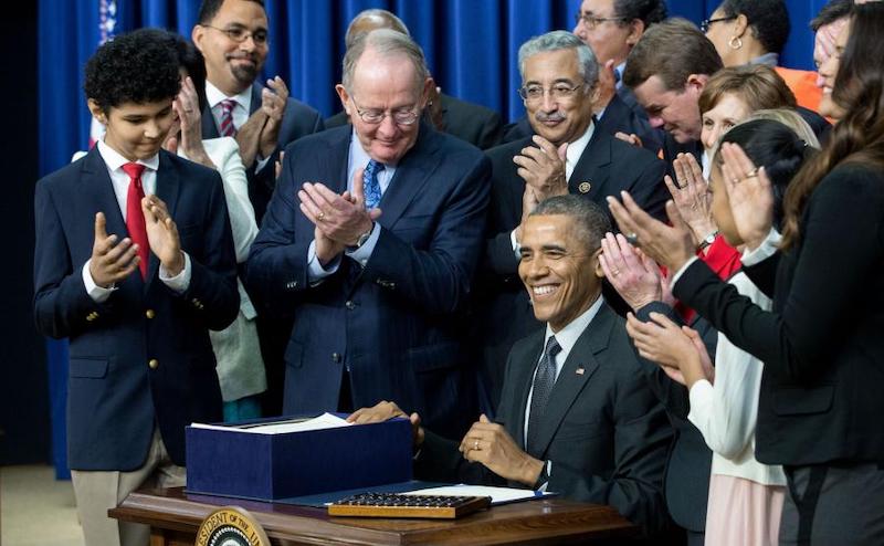 prsident obama signing the ESSA into law with students and cabiet members behind him