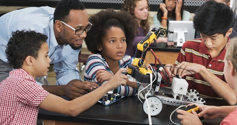 a group of students working with a robot in the classroom as a teacher helps