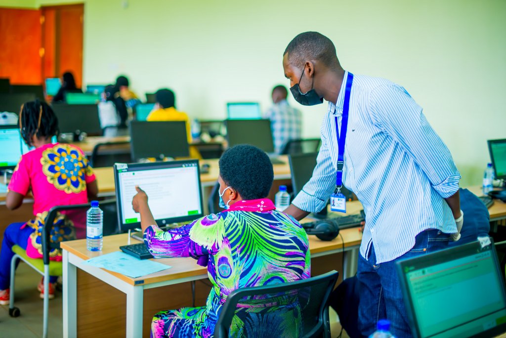 a teacher looks on and helps a student with typing on a computer